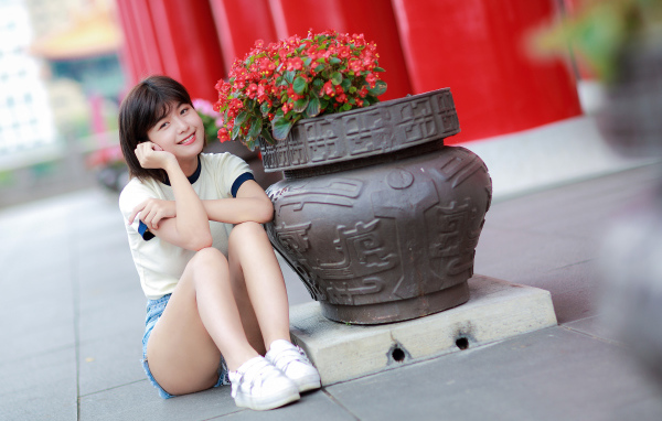 Улыбающаяся азиатка сидит у клумбы с цветами