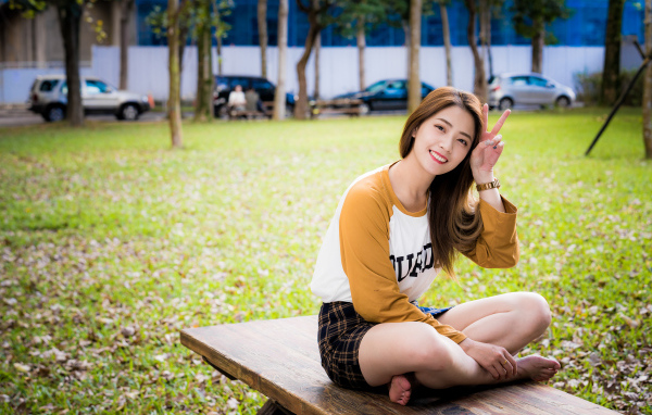 Улыбающаяся девушка азиатка сидит на лавке в парке 