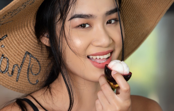 Улыбающаяся азиатка в шляпе с фруктом в руке