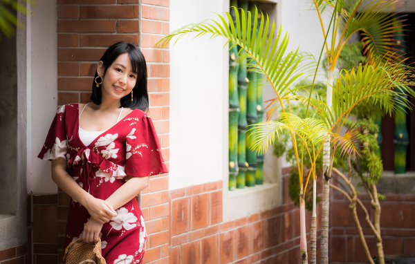 Улыбающаяся азиатка в красном платье стоит у стены 