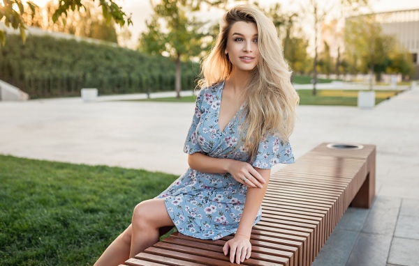 Улыбающаяся блондинка сидит на лавке 