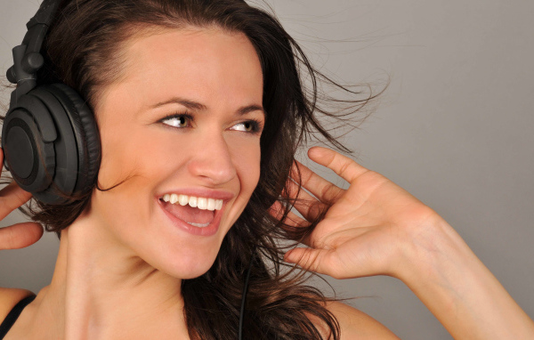 Улыбающаяся девушка в наушниках на сером фоне 