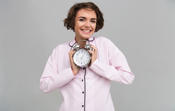 Улыбающаяся девушка в пижаме держит будильник 