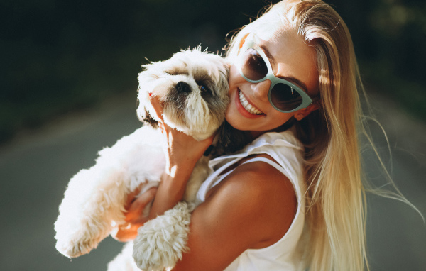 Улыбающаяся девушка в солнечных очках с собакой на руках