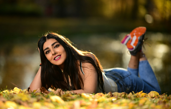 Улыбающаяся девушка модель лежит на земле с опавшими листьями