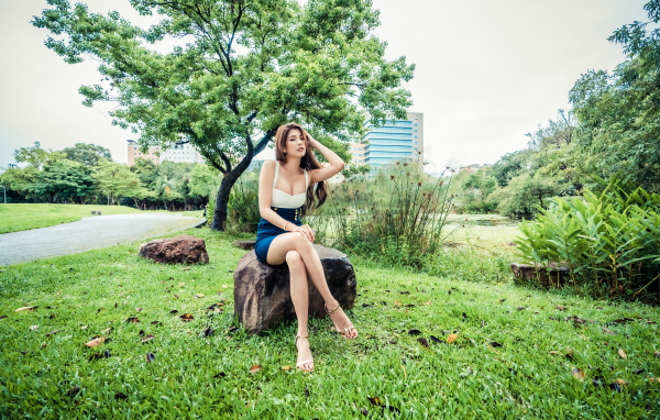 Эффектная девушка азиатка сидит на камне в парке