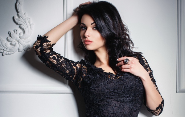 Эффектная брюнетка в черном платье у стены