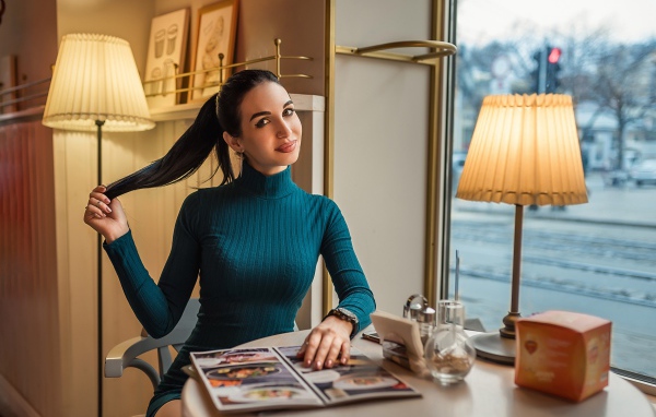 Стильная девушка в платье сидит в кафе у окна