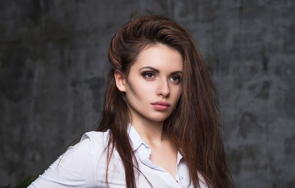 Стильная девушка в белой рубашке на фоне серой стены 