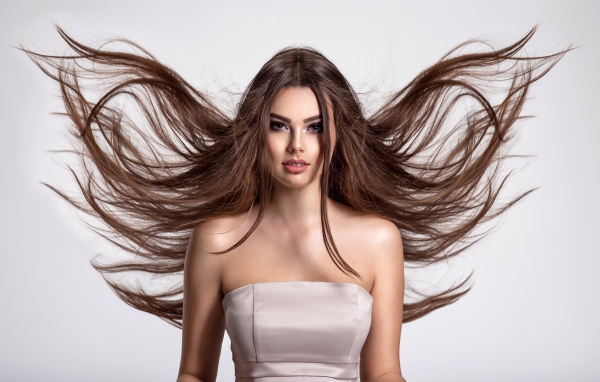 Ветер развивает волосы красивой девушке шатенке на сером фоне