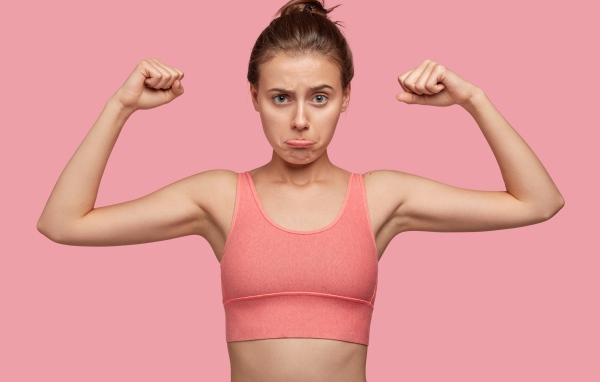 Расстроенная девушка без накаченных рук на розовом фоне