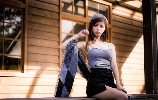 Молодая девушка азиатка в короткой юбке сидит на подоконнике 