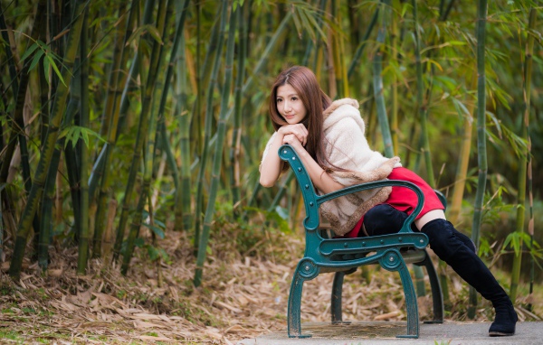 Молодая девушка азиатка сидит на зеленой лавке 