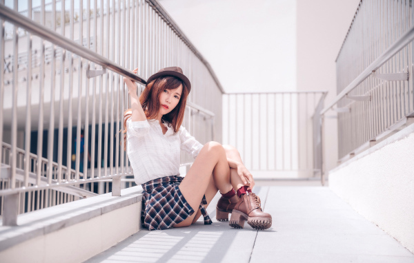 Молодая азиатка в короткой юбке сидит у перил 