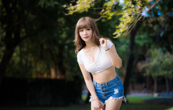 Молодая азиатка в белом топе и синих шортах  в парке