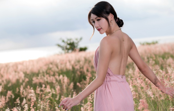 Молодая азиатка в розовом платье гуляет по полю с колосьями