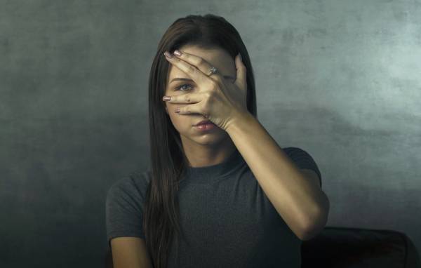 Молодая девушка закрыла лицо рукой на сером фоне