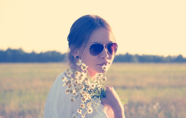 Молодая девушка в солнечных очках с букетом ромашек на поле