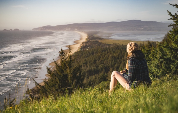 Молодая девушка сидит на зеленой траве на фоне моря