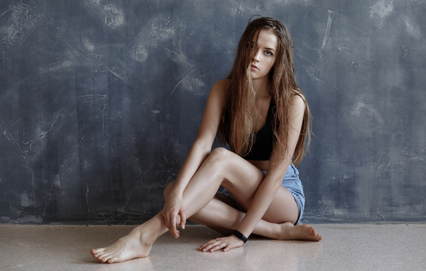 Молодая девушка с мокрыми волосами сидит у стены 