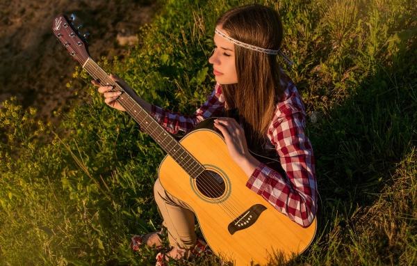 Молодая девушка хиппи сидит с гитарой на траве 