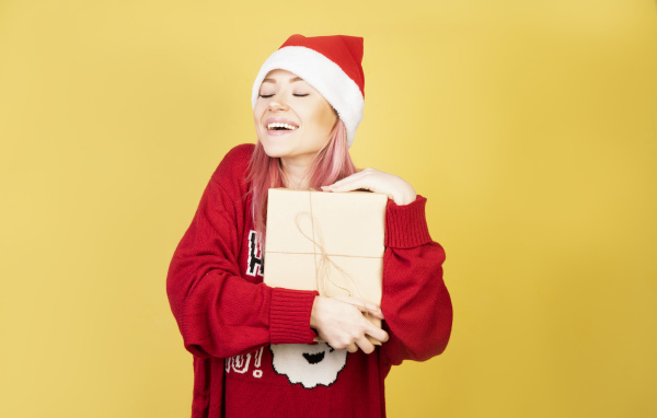 Улыбающаяся девушка в красном свитере с подарком на желтом фоне