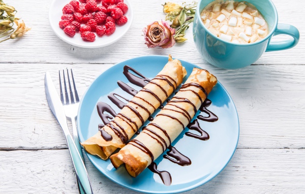 Тонкие блины с шоколадом на столе с ягодами малины и какао 