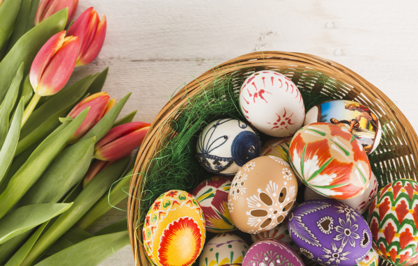 Разноцветные крашеные яйца в корзине с букетом тюльпанов на Пасху