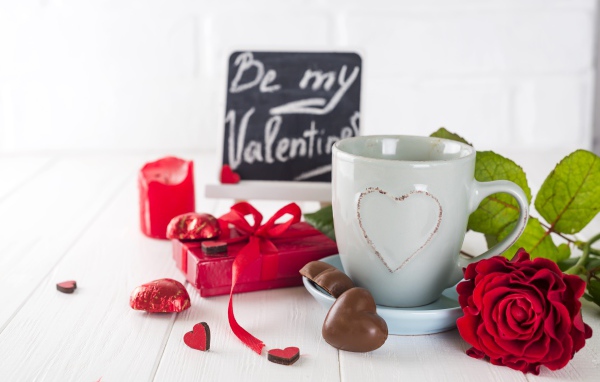 Белая чашка с конфетами и красной розой на столе в подарок на 14 февраля