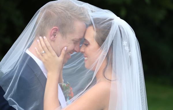 Жених и невеста стоят под белой фатой