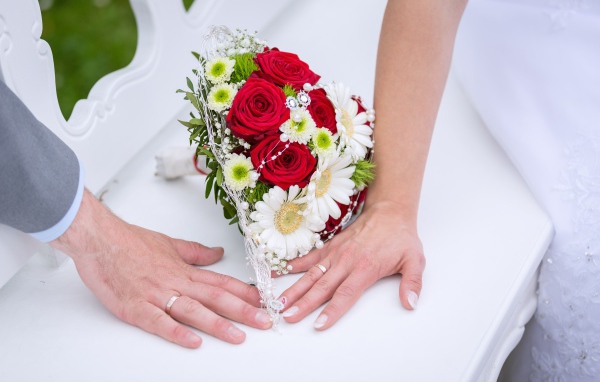 Две руки с обручальными кольцами и свадебным букетом