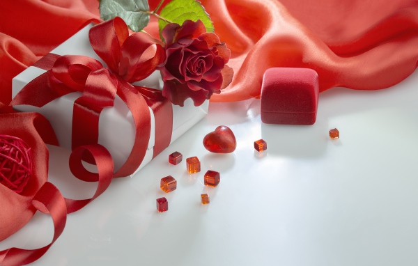 Подарки на белом столе с розой и красной тканью