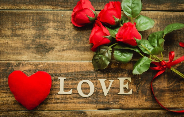 Надпись LOVE на столе с розами и красным сердцем