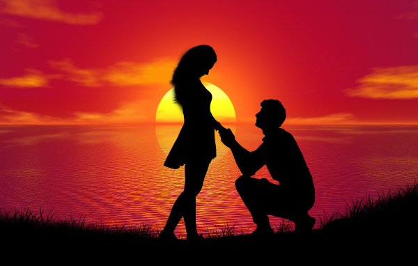 Парень делает девушке предложение на фоне заката у моря