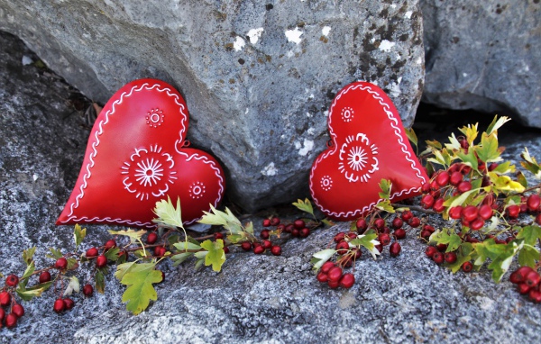 Два сердца лежат у камня с красными ягодами
