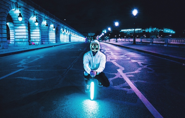 A guy in a luminous mask sits with a neon lamp on the road
