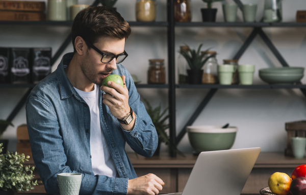 Мужчина с ноутбуком ест яблоко в кафе 