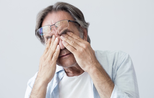 Elderly man rubs his eyes on a gray background