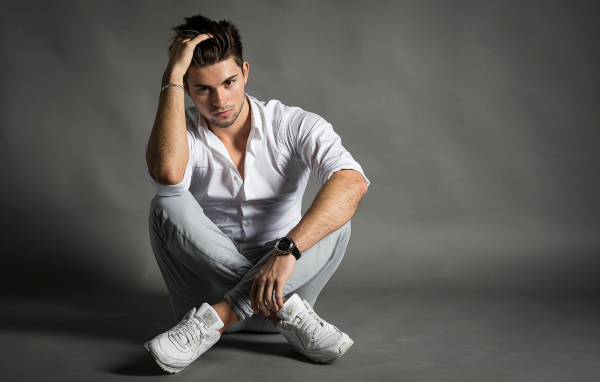 Handsome young man in white shirt sits by the wall