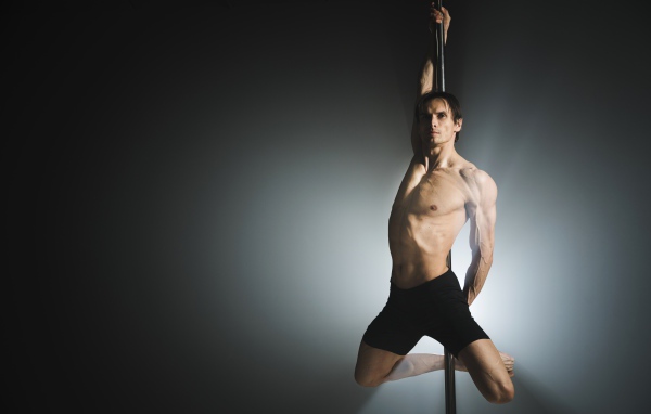 Мужчина танцует на пилоне на сером фоне