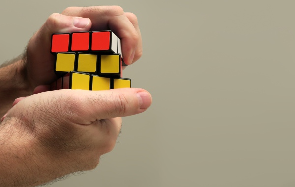 Кубик Рубика в руках мужчины на сером фоне