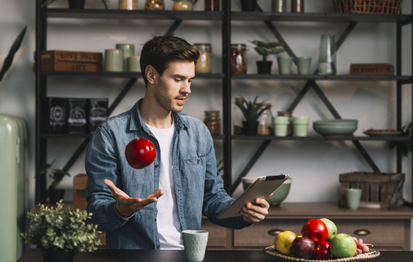 Молодой мужчина с планшетом и яблоком в руке 