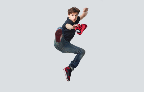 Молодой актер Том Холланд в прыжке на сером фоне
