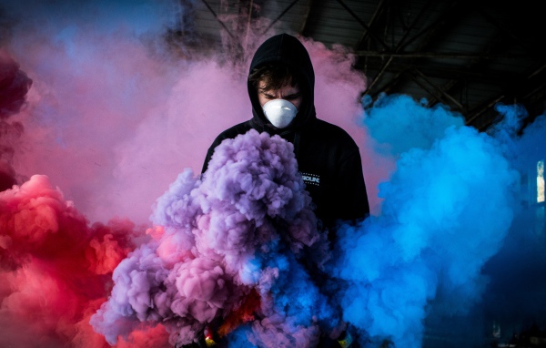 Мужчина в маске с разноцветными дымовыми шашками