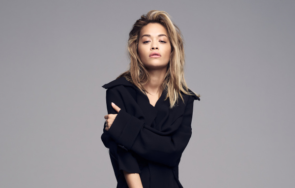 Певица Рита Ора в черном наряде на сером фоне