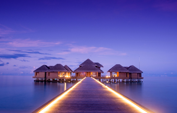 Мост с подсветкой идет к домам на сваях в океане