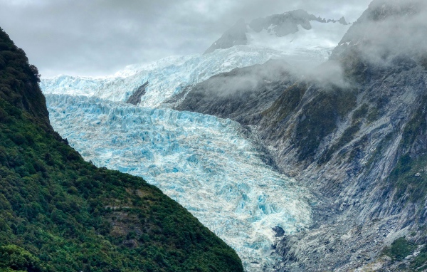 Blue glacier between rocks under stormy sky