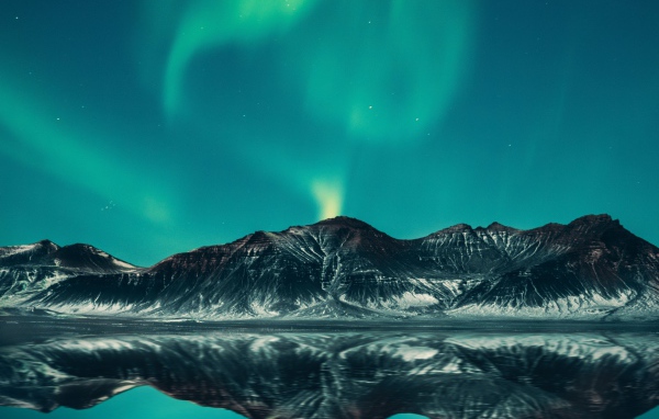 Зеленое северное сияние в небе над горами у озера 