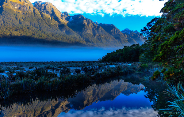 Горы и небо отражаются в голубой воде озера 
