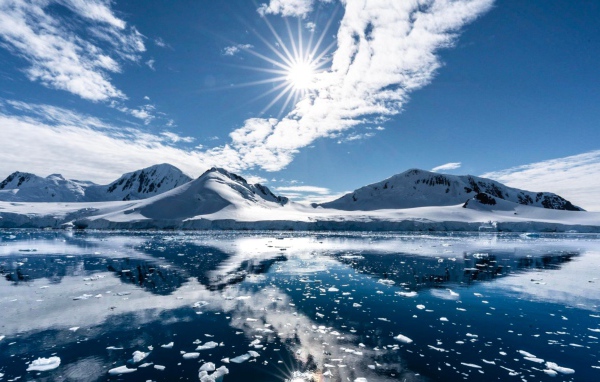 Белые облака в солнечном небе отражаются в озере у заснеженных гор 